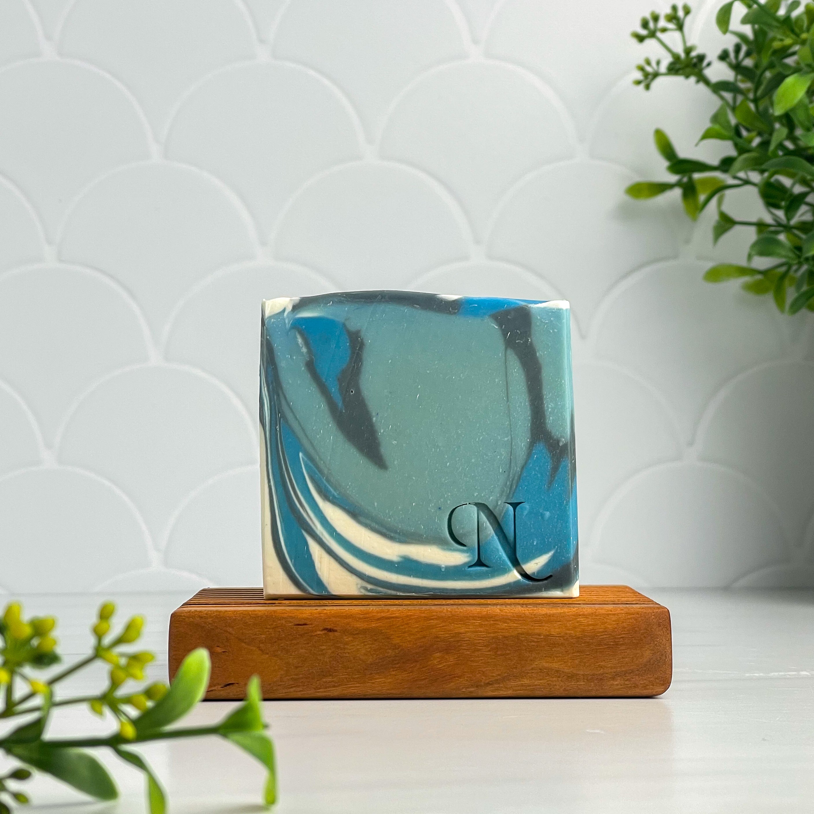 Aqua Artisan Soap - White, black and blue soap sitting on a soap dish with some greenery framing the picture